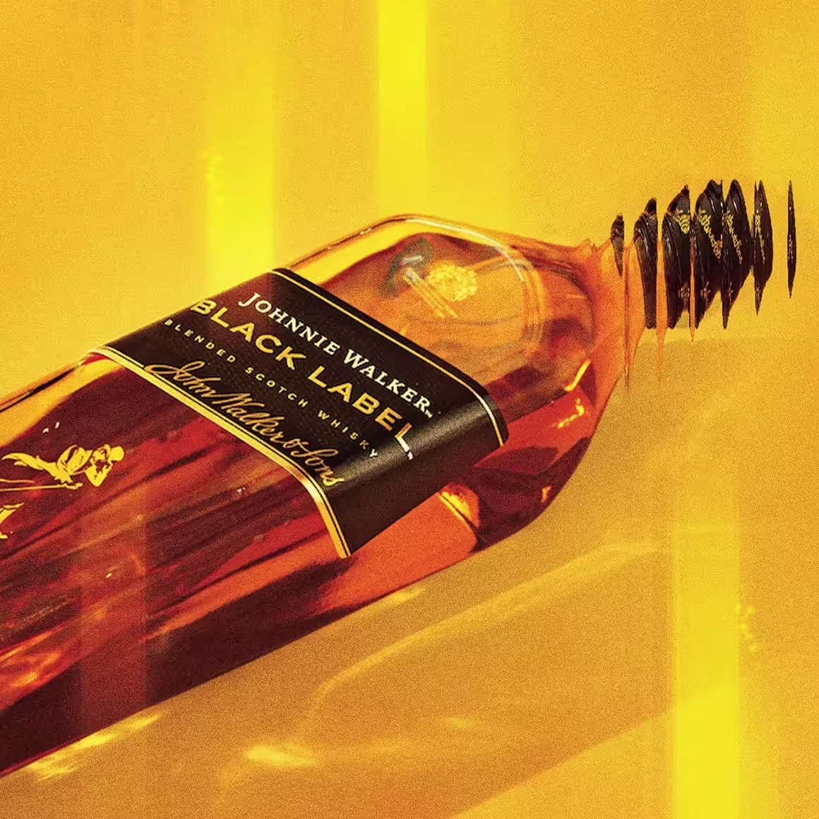 Una botella de whisky Johnnie Walker Black Label con un lazo negro alrededor del cuello y una cinta, sobre un vibrante fondo degradado naranja y amarillo.