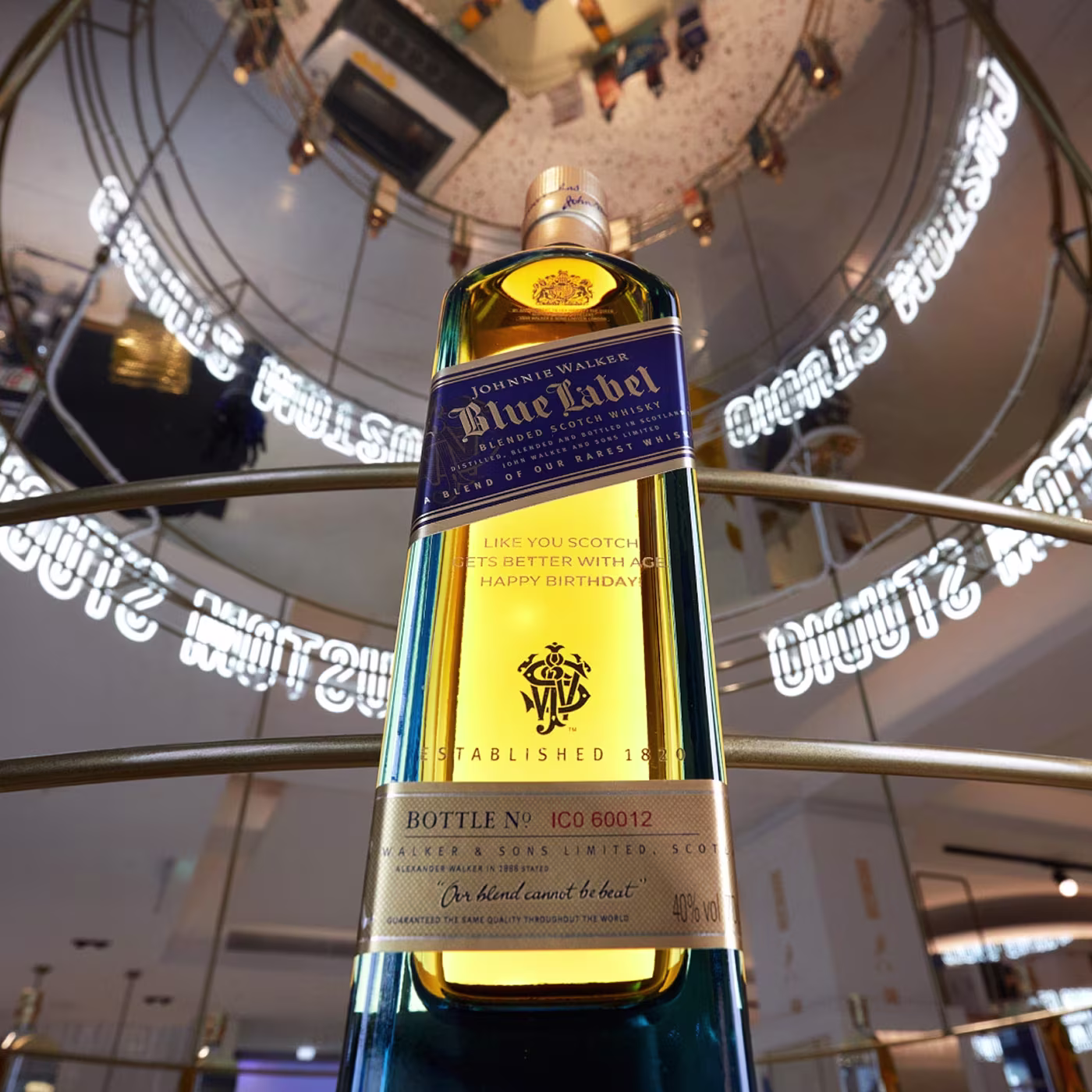 A Johnnie Walker Blue Label whisky bottle displayed in a modern, mirrored setting with neon signage.