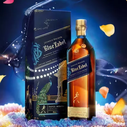 A bottle of Johnnie Walker Blue Label whisky stands beside an ornate, dark blue box with gold and peacock designs. Colorful flower petals float around on a deep, vibrant background.