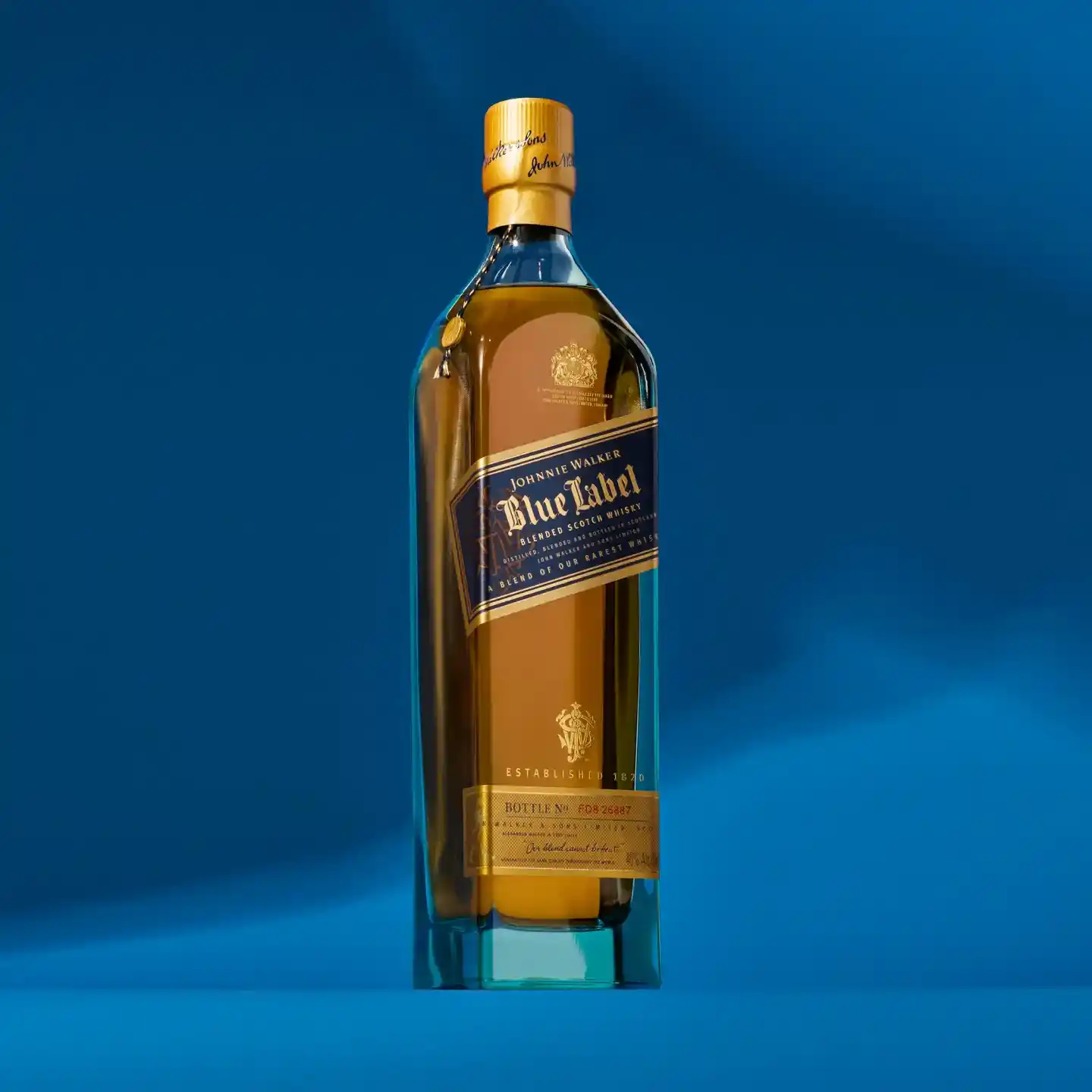 Una botella de whisky Johnnie Walker Blue Label sobre un fondo azul. La botella presenta una etiqueta azul marino y dorada con texto y emblemas detallados. El fondo y la botella crean un tema azul armonioso.