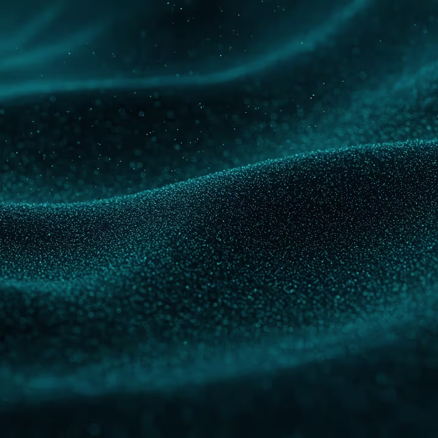 A close-up image of teal-colored fine particles forming smooth, wavy patterns, resembling sand dunes or flowing fabric, with glowing dots scattered throughout against a dark background.