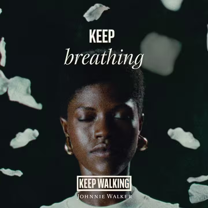 A person with closed eyes stands against a dark background with white petals falling. The words KEEP breathing appear, along with the Johnnie Walker logo and the phrase KEEP WALKING at the bottom.