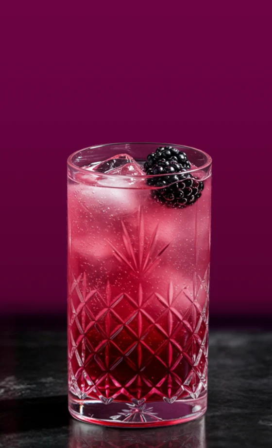 A tall, clear glass with a decorative pattern holds a vibrant pink cocktail, topped with ice cubes and garnished with blackberries. The background is a rich, deep purple, providing contrast to the drink.