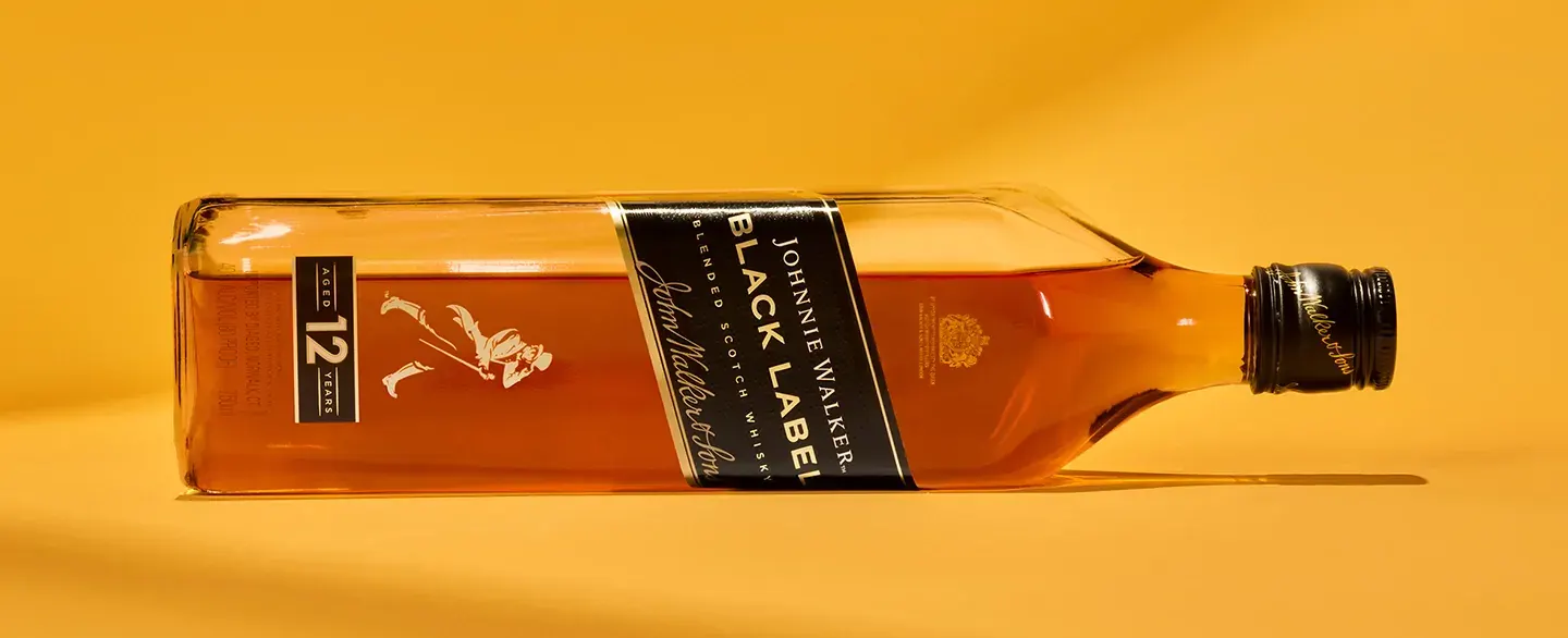 A bottle of Johnnie Walker Black Label 12 year old Scotch whisky lies on a yellow surface. 