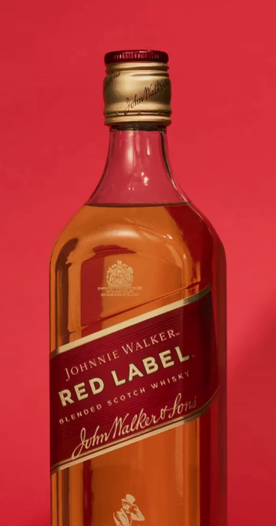 Una botella de whisky escocés Johnnie Walker Red Label Blended sobre fondo rojo. La etiqueta lleva el nombre de la marca y el logotipo en dorado. El tapón es dorado con el nombre de la marca en relieve.