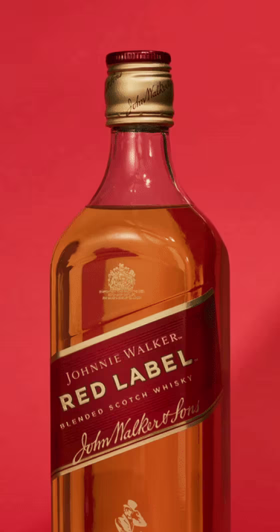 Một chai rượu Scotch Whisky pha trộn Johnnie Walker Red Label trên nền đỏ. Nhãn có tên thương hiệu và logo bằng vàng. Mũ màu vàng có in nổi tên thương hiệu.