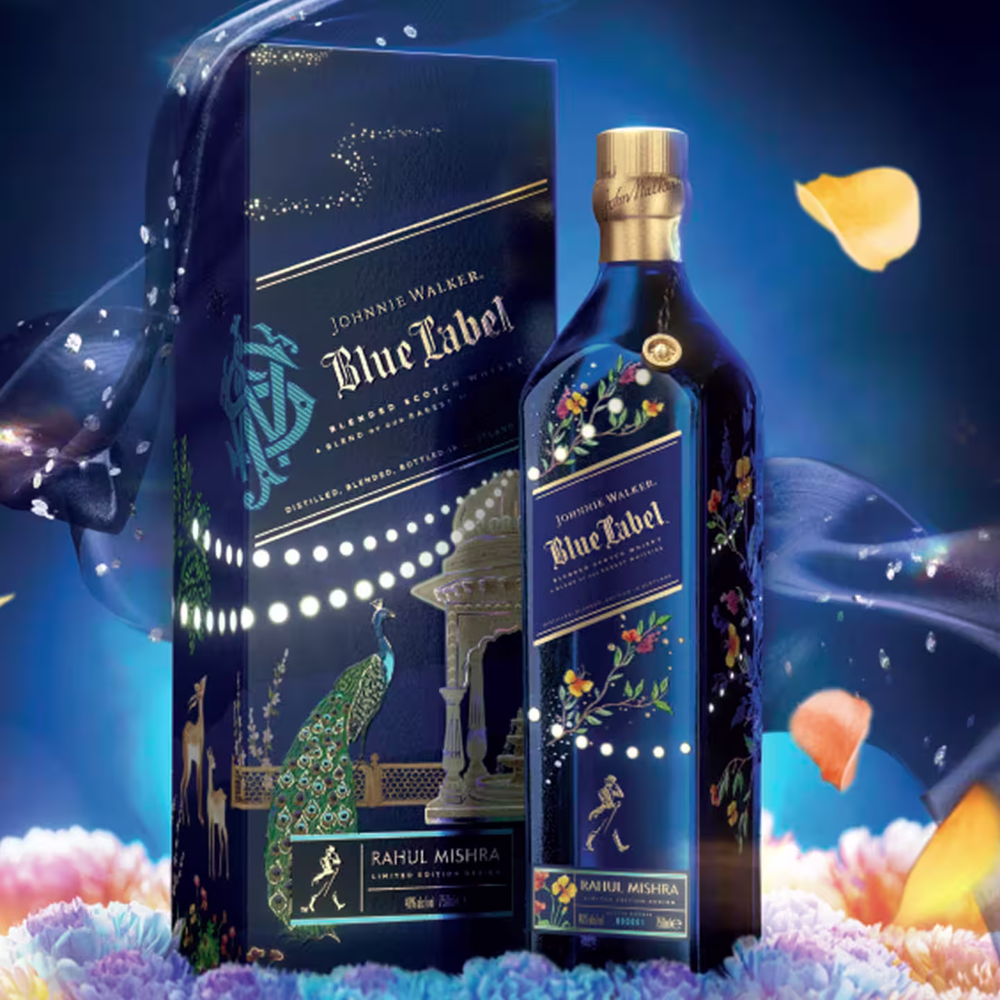 A Johnnie Walker blue label x rahul mishra limited edition design and its decorative box, both featuring intricate, colourful patterns and floral designs. The background includes blue silk fabric, petals, and soft glowing lights for an elegant effect.