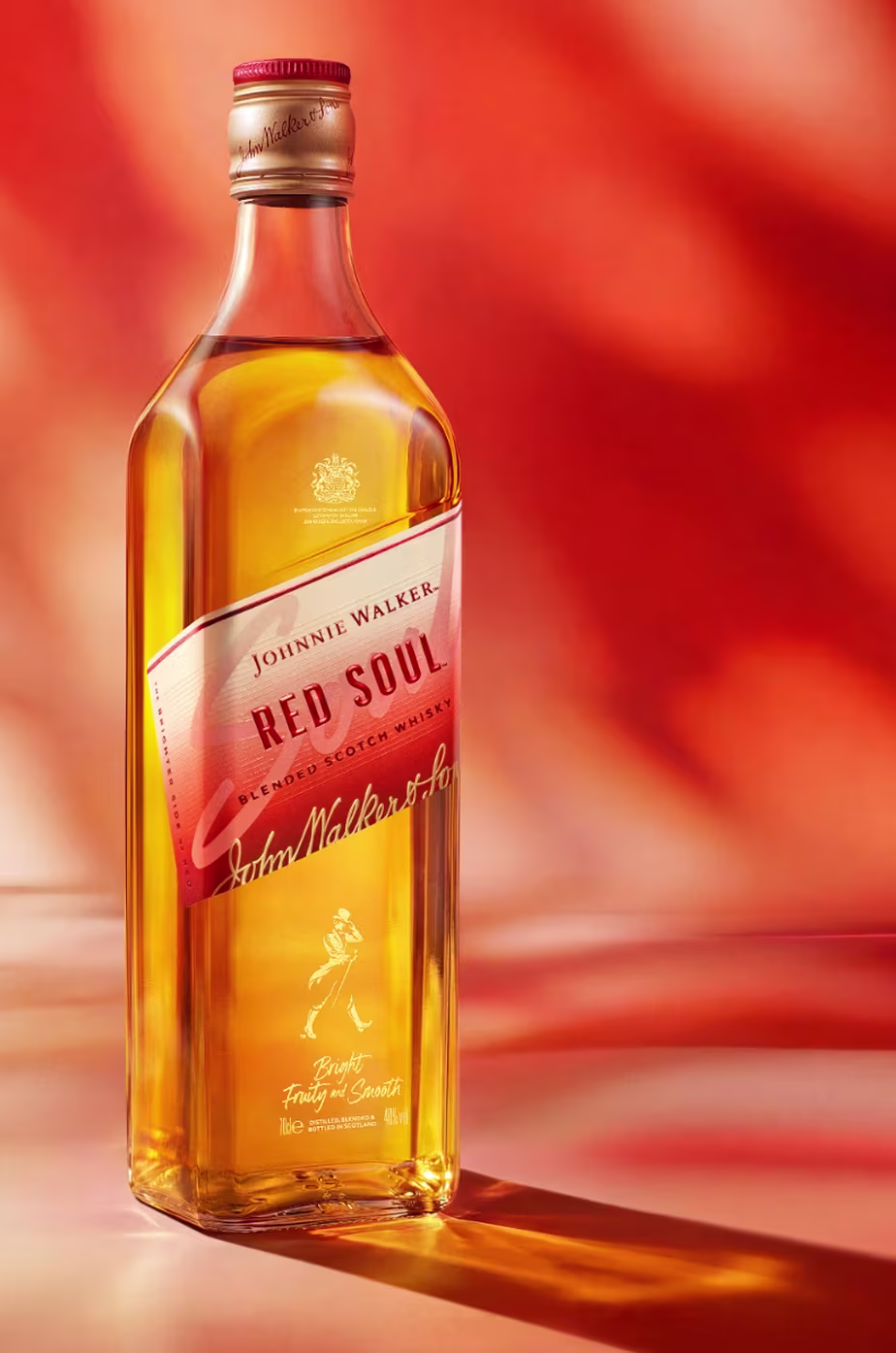 Láhev whisky Johnnie Walker Red Soul stojí na podkladu s hřejivým, červeno-oranžovým abstraktním pozadím.