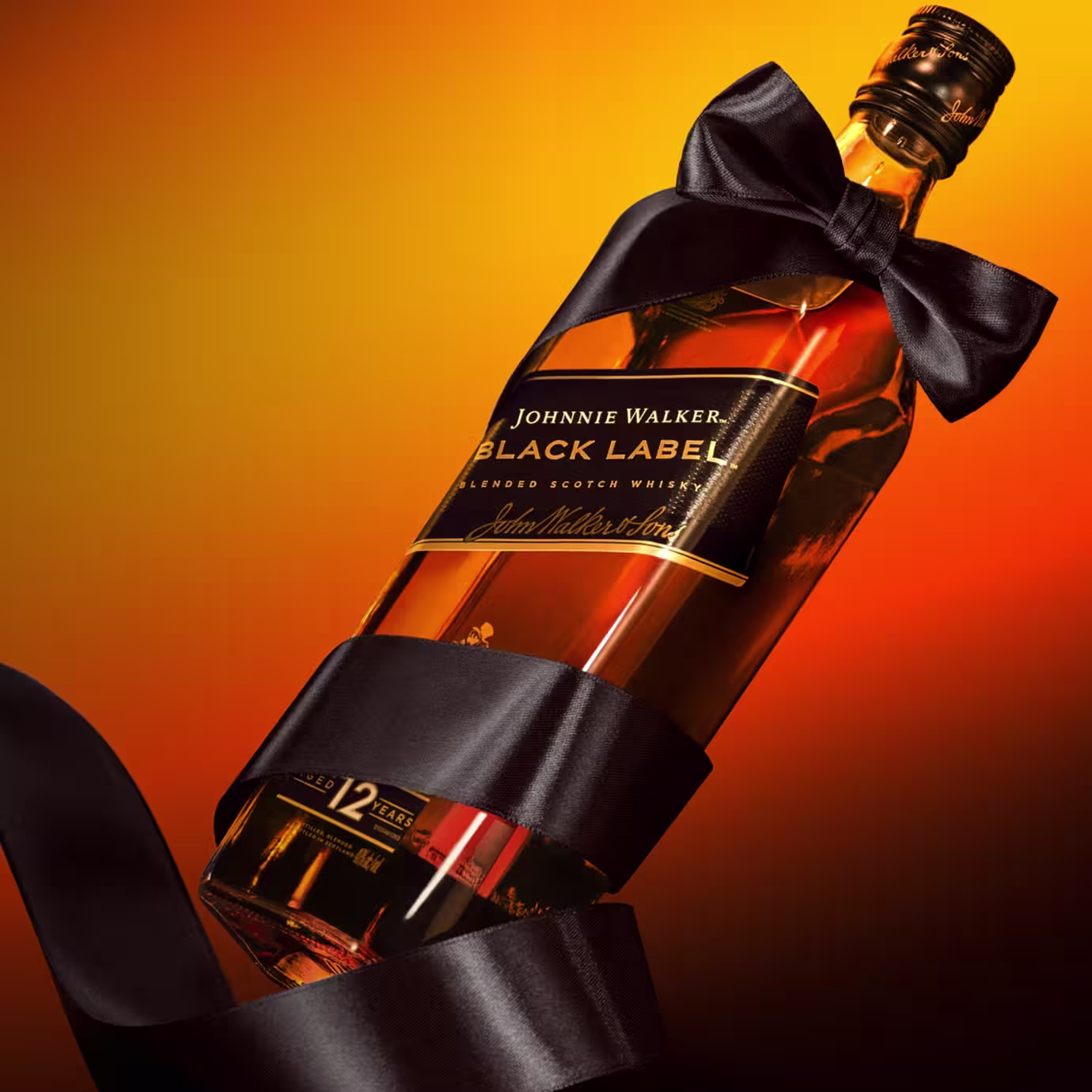 オレンジと黄色のグラデーションの背景に、蝶結びした黒いサテンのリボンで包まれたジョニーウォーカー ブラックラベル ウイスキーのボトルが映えます。