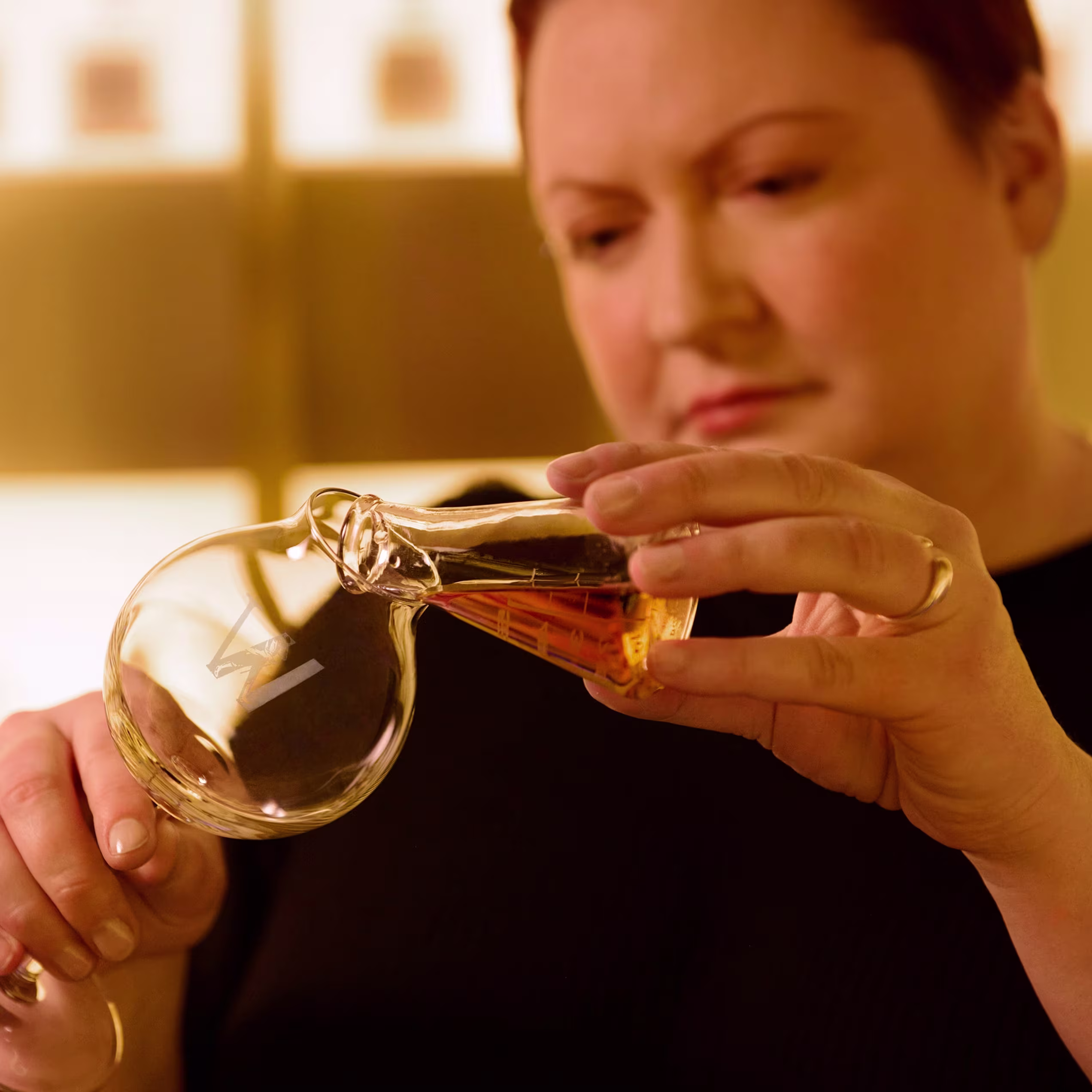 A person carefully pouring amber liquid from a glass vessel.