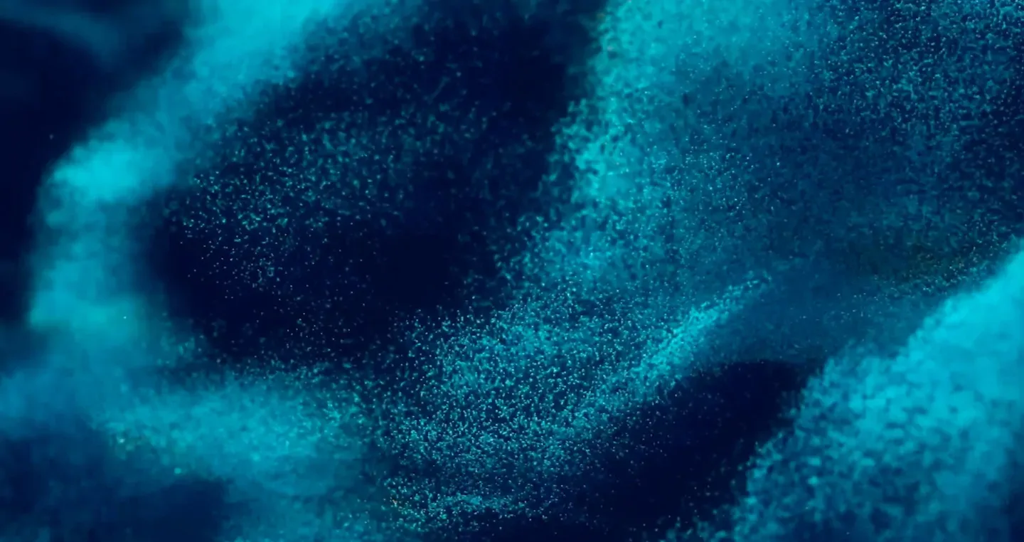 A swirling pattern of vibrant teal and dark blue particles creates a dynamic, abstract texture reminiscent of ocean waves or clouds. The particles blend smoothly, forming a mesmerizing and fluid motion.