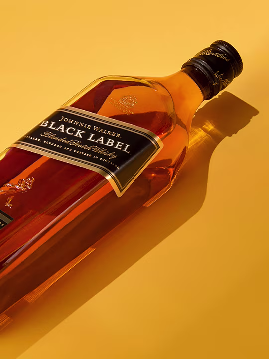Johnnie Walker Black Label 威士忌酒瓶倒立在芥末黃背景上。光線從瓶子反射出來，在左側投下陰影。瓶子上似乎有標籤，但文字不清晰。