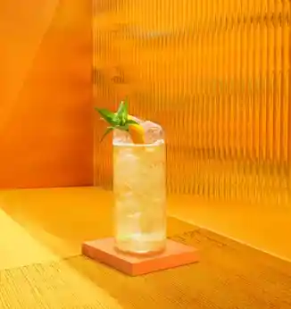 A hand is placing an orange slice into a cocktail glass with a bottle of Johnnie Walker Black Label in the background. 
