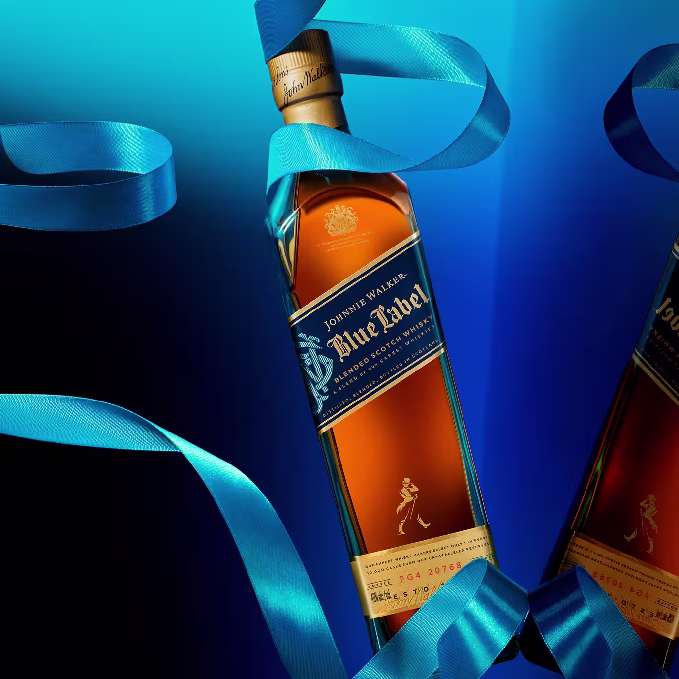 A bottle of Johnnie Walker Blue Label whisky is wrapped with a flowing blue ribbon against a blue gradient background, with part of a second bottle visible on the right side.