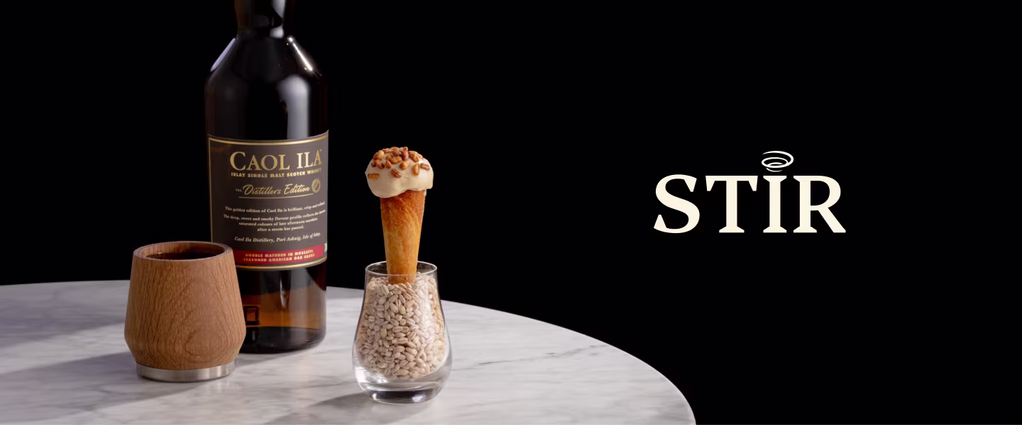 Một chai rượu whisky Caol Ila, một chiếc cốc gỗ, và một món tráng miệng trong ly trên một bàn đá cẩm thạch.