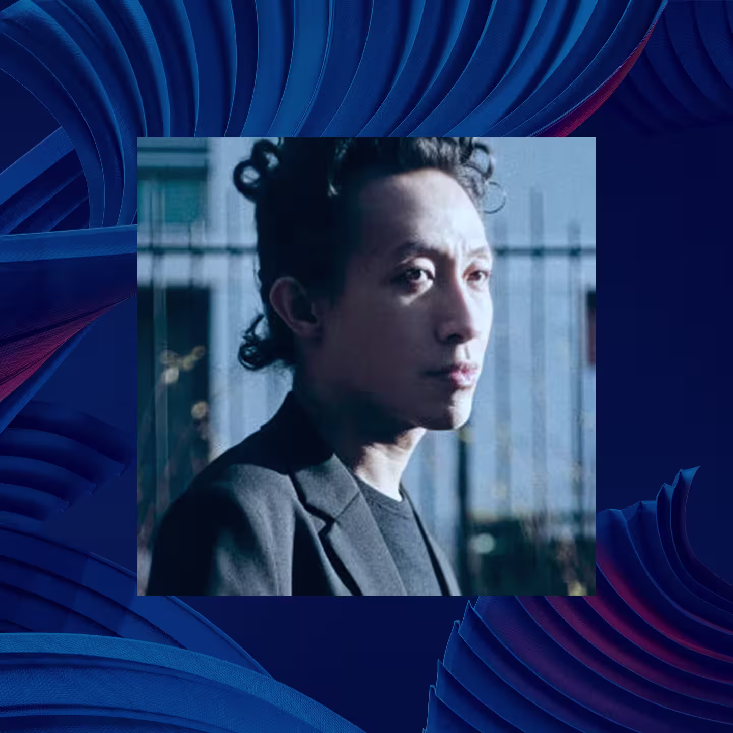 Robert Wun with curly hair and a serious expression stands outside, wearing a dark jacket; the image has a blue abstract patterned border.