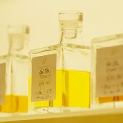 Square glass bottles filled with amber liquid are arranged in a soft, warm light. The bottles have handwritten labels featuring decorative typography.