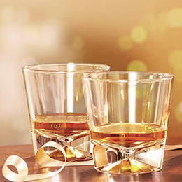 Glasses with amber liquid, warm bokeh lights, festive atmosphere, ribbon nearby.