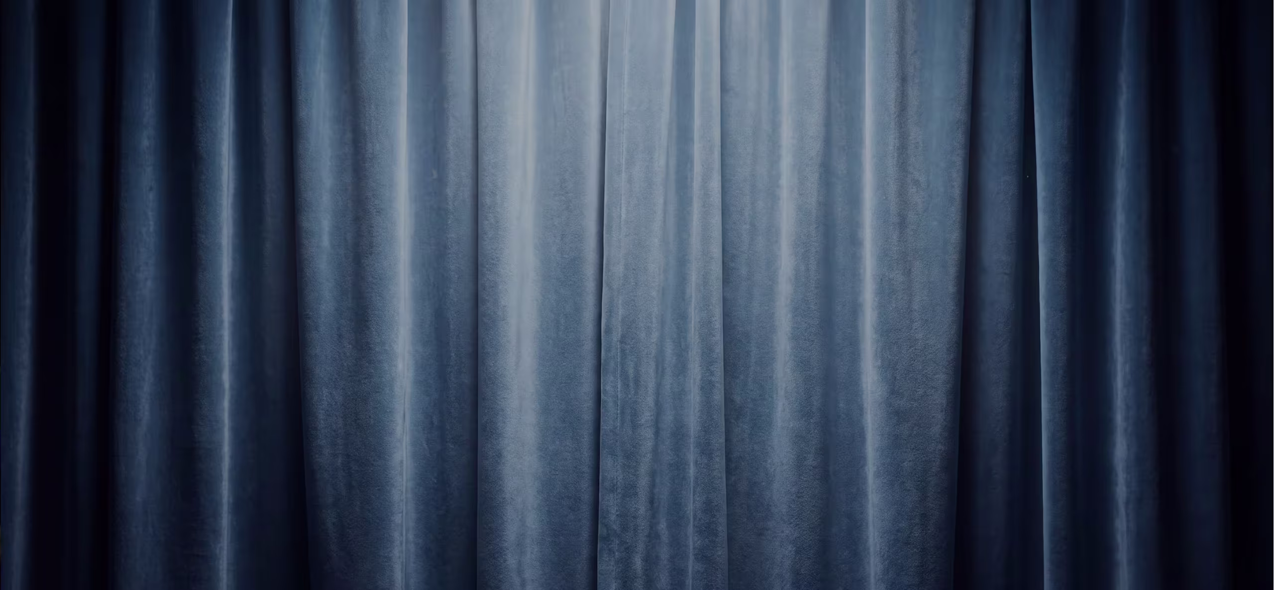 Closed blue velvet curtains with soft vertical folds, evenly lit with a subtle glow from above.