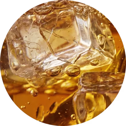 Close-up van ijsblokjes die drijven in een goudbruine vloeistof, met bubbels die naar de oppervlakte stijgen.