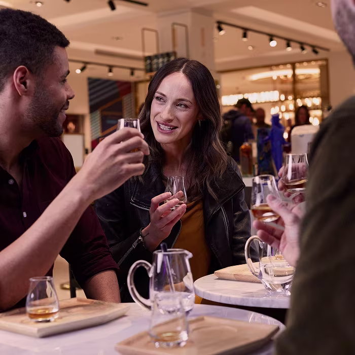 Three people sit at a table in a modern bar, smiling and enjoying drinks together.