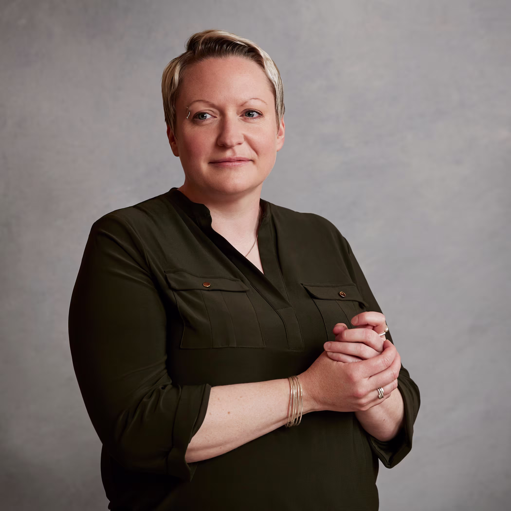 Portrait of Dr. Emma Walker, Johnnie Walker Master Blender, in a dark green shirt with hands clasped against a grey backdrop.