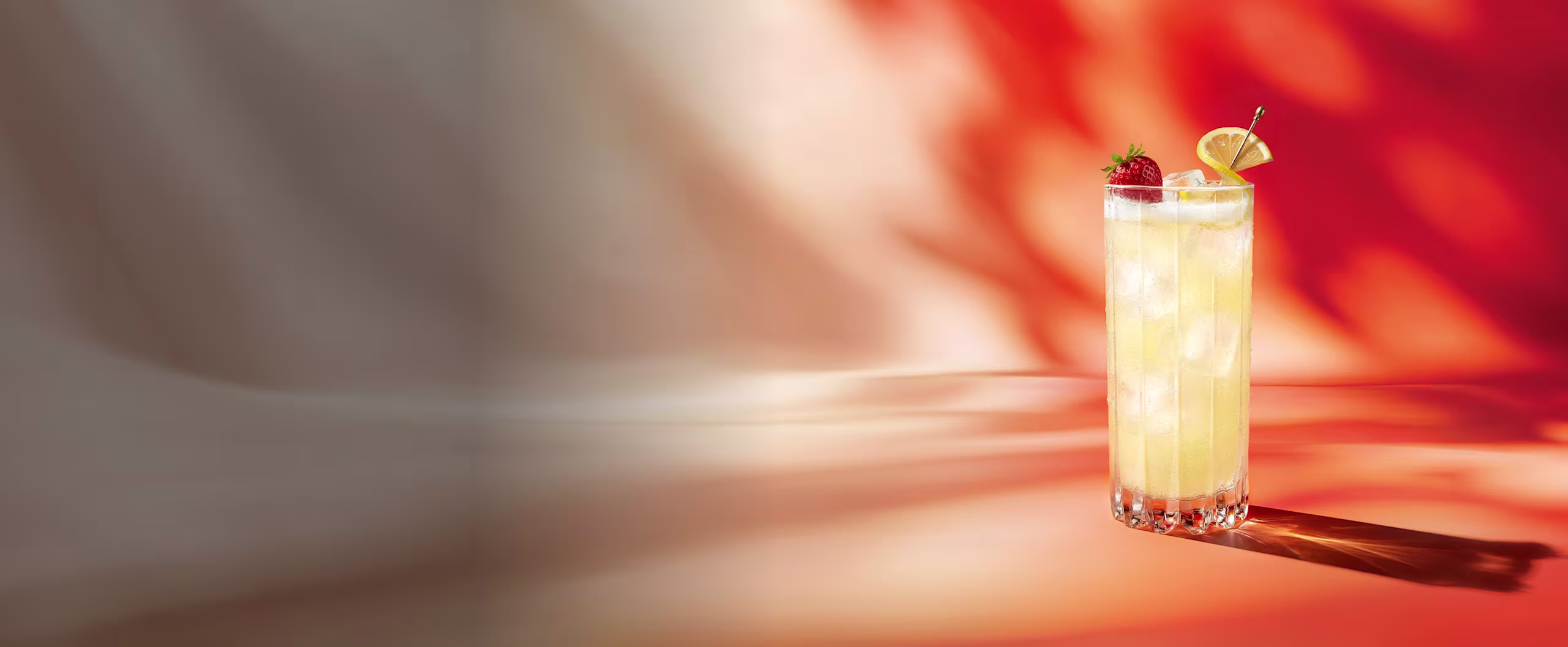 A tall glass of iced lemonade garnished with a strawberry and lemon slice on a colourful, sunlit surface.