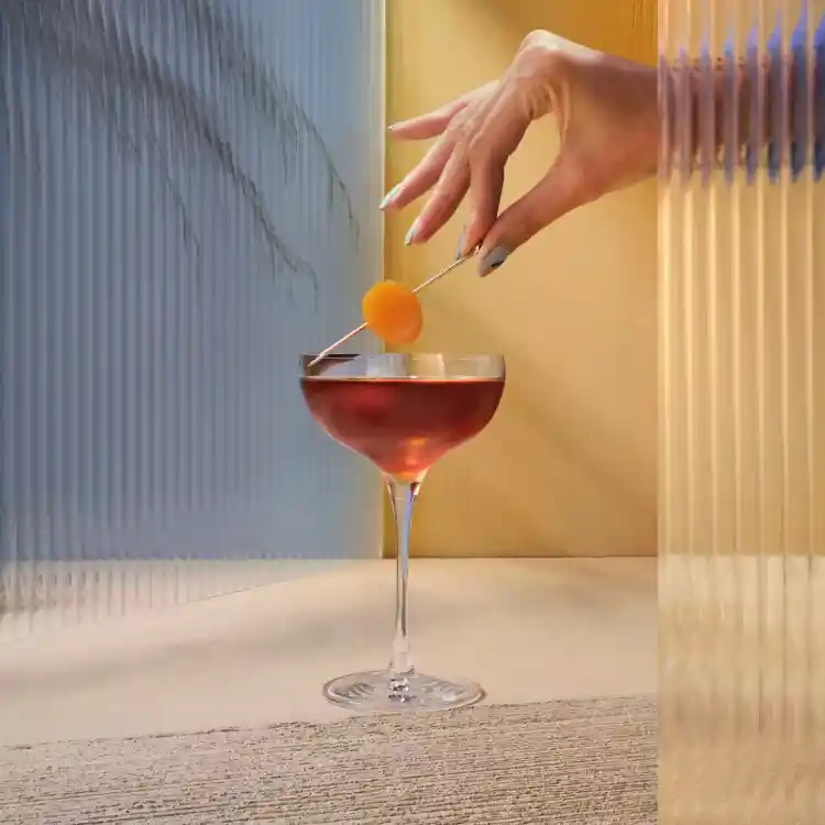 A hand is holding a cocktail garnish over a martini glass. 
