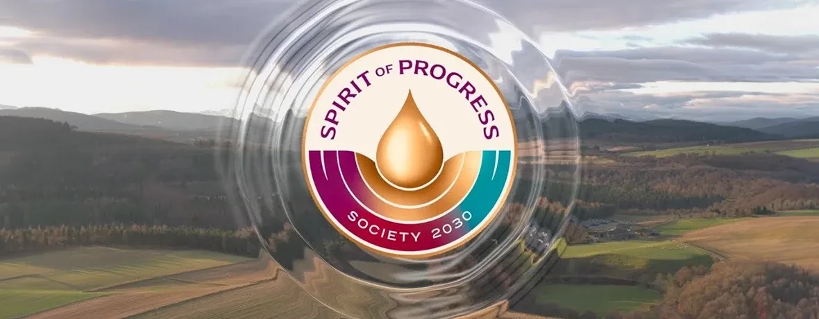 A circular logo with a gold droplet in the center and the words Spirit of Progress Society 2030 overlays a blurred aerial view of fields, forests, and distant hills.
