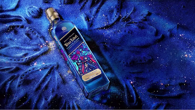 A bottle of Johnnie Walker Blue Label Festive Blend whiskey against a textured blue background.