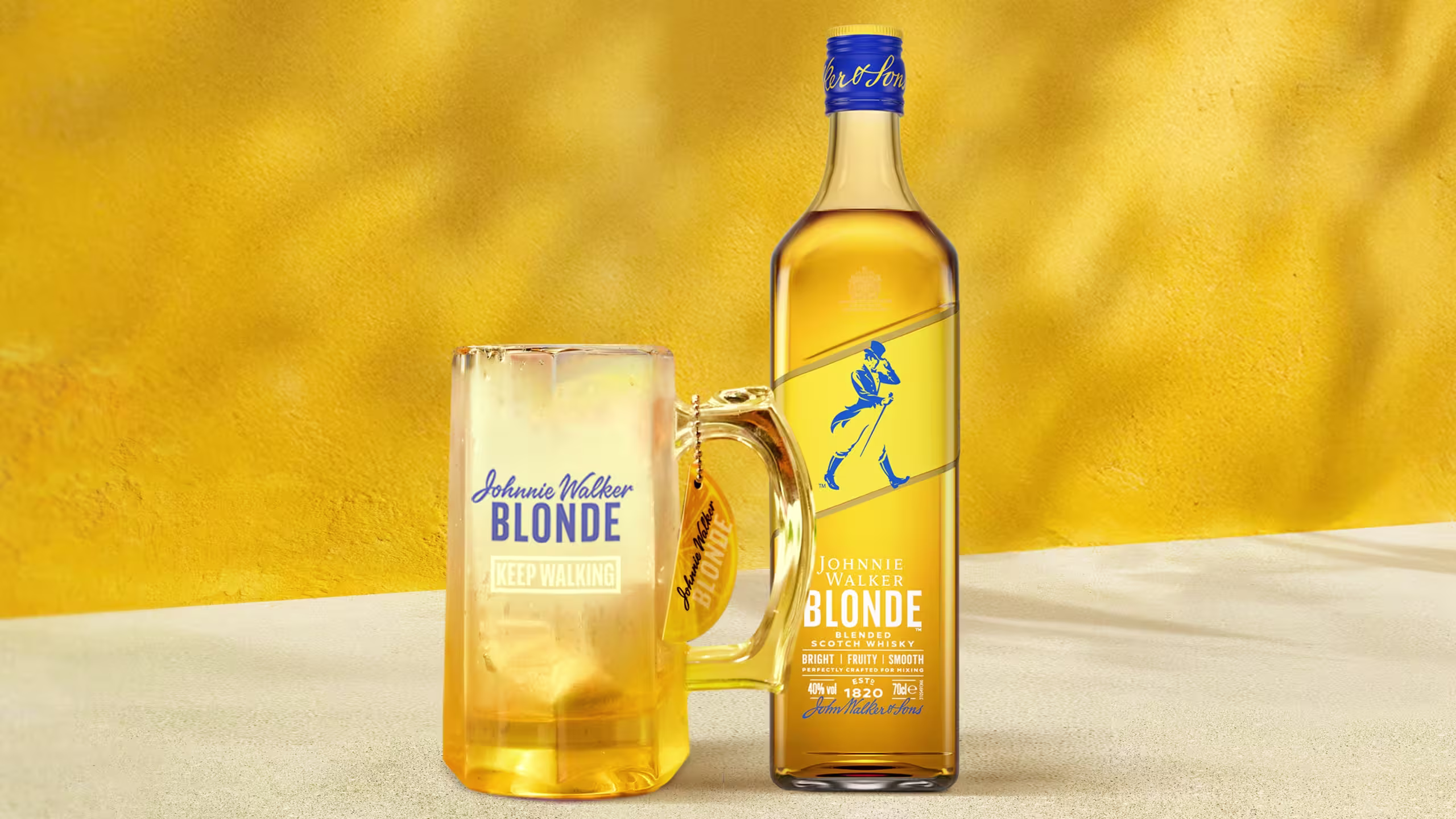 一瓶尊尼獲加金色威士忌旁邊是一個裝滿冰鎮威士忌的磨砂玻璃杯,背景為亮黃色。瓶子標籤上印有標誌性的行走人標誌。
