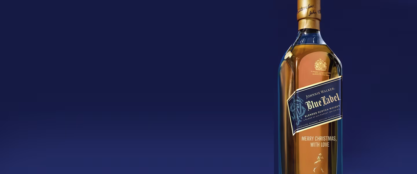 Een fles Johnnie Walker Blue Label whisky tegen een donkerblauwe achtergrond, met het etiket en de gouden dop zichtbaar en de tekst Merry Christmas With Love gegraveerd op de fles.