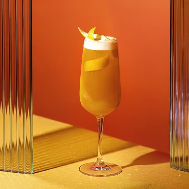 A close-up of a champagne flute being filled with a bubbly golden drink, next to a bottle of Johnnie Walker Blue Label whisky on a table with a white tablecloth and a dark vase with flowers.