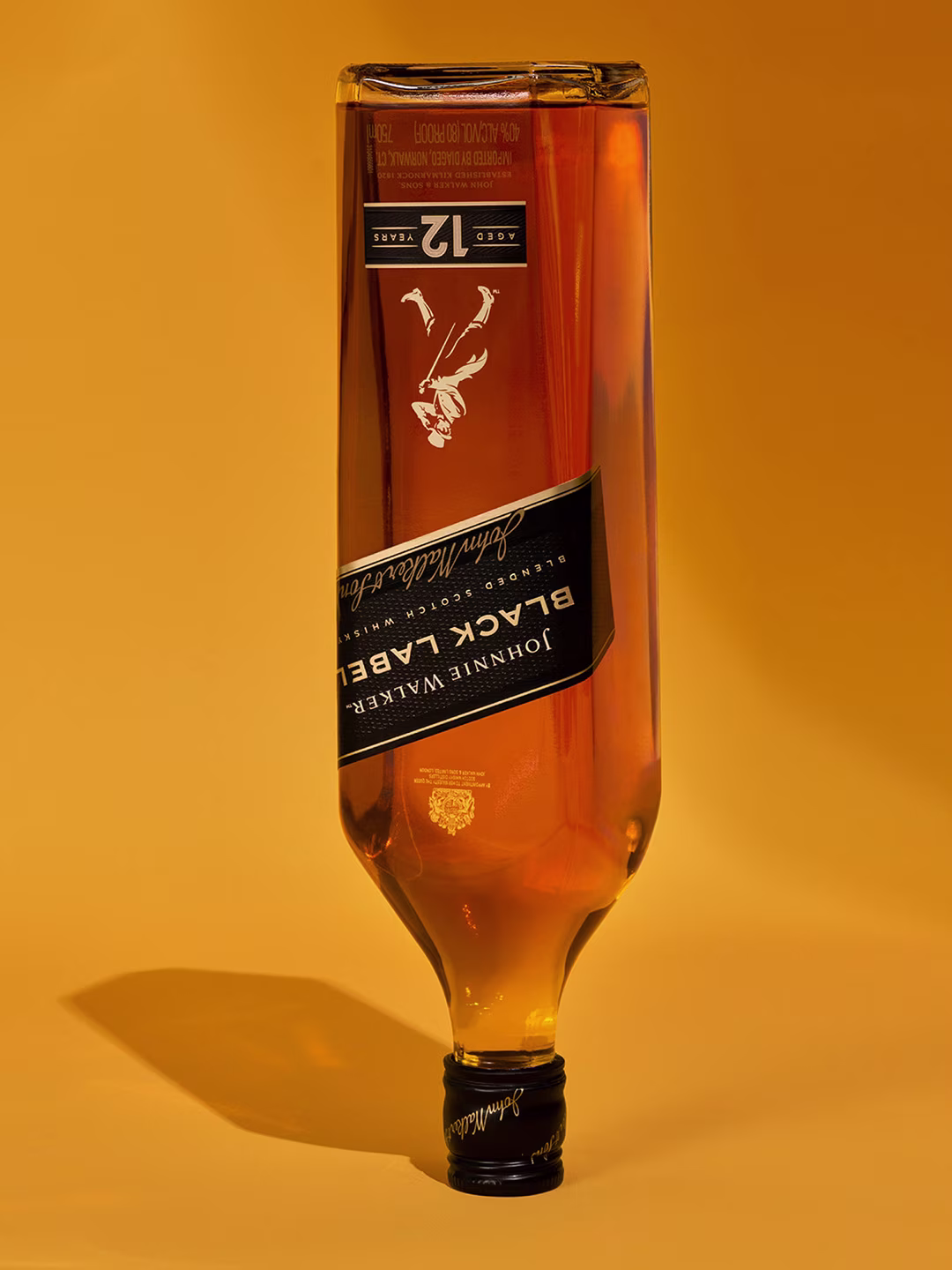 Black Label A bottle of Johnny Walker Black Label whisky is upside down on a yellow background. The label displays Aged 12 Years, with a shadow cast on the surface.