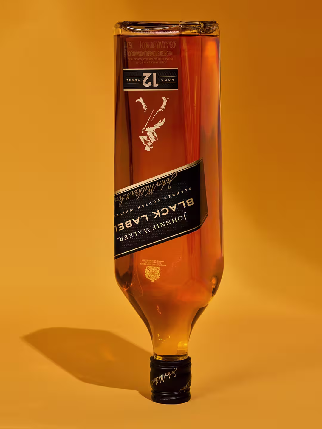 Una botella de whisky con etiqueta negra se muestra boca abajo sobre un fondo amarillo cálido. La etiqueta presenta una figura estilizada y el número 12, que indica la edad. Se ven sombras en la superficie.