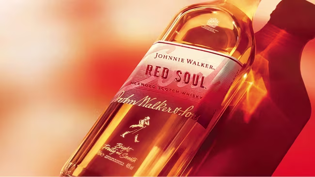 Láhev míchané skotské whisky Johnnie Walker Red Soul na teplém, načervenalém pozadí.