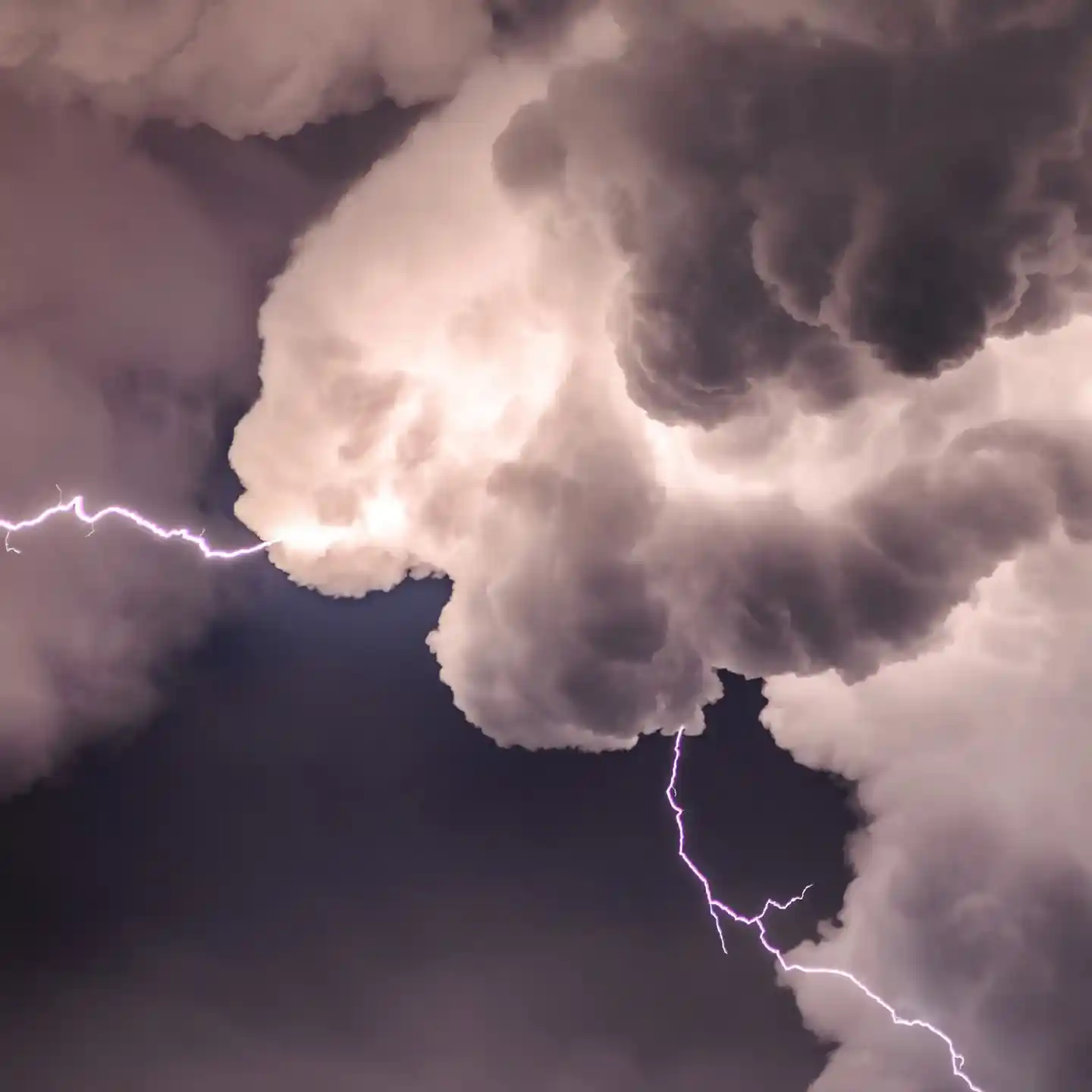  A dramatic scene of dark, dense clouds illuminated by a bright streak of lightning, creating a contrast against the dark sky. The cloud formations are textured and swirling, emphasizing the stormy atmosphere.