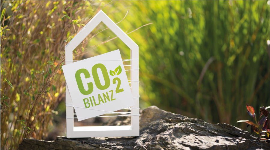 weisses Haus im Garten mit Schild CO2 Bilanz