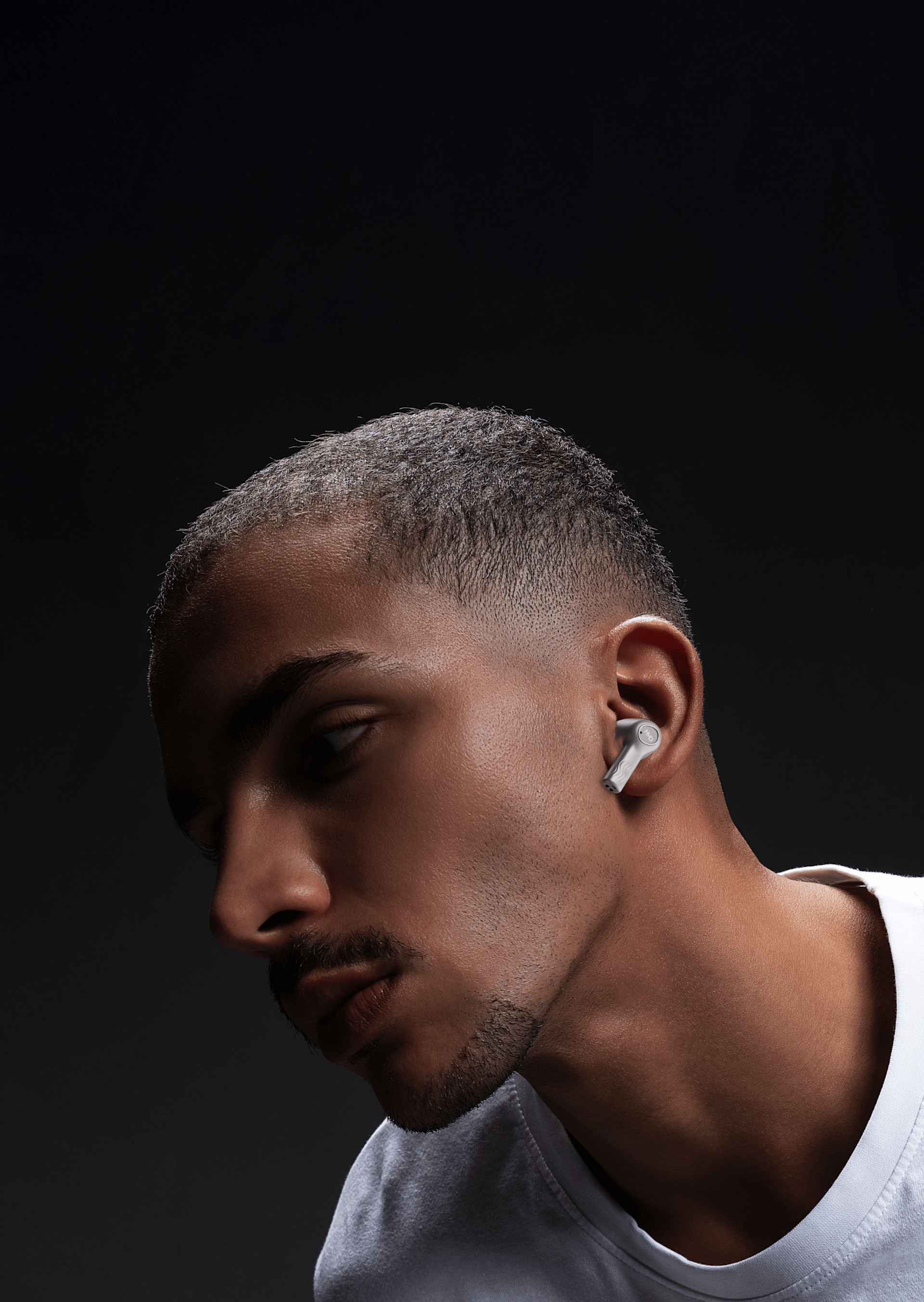 Man wearing white HMD X50 Pro earbuds, looking down, against a dark background.