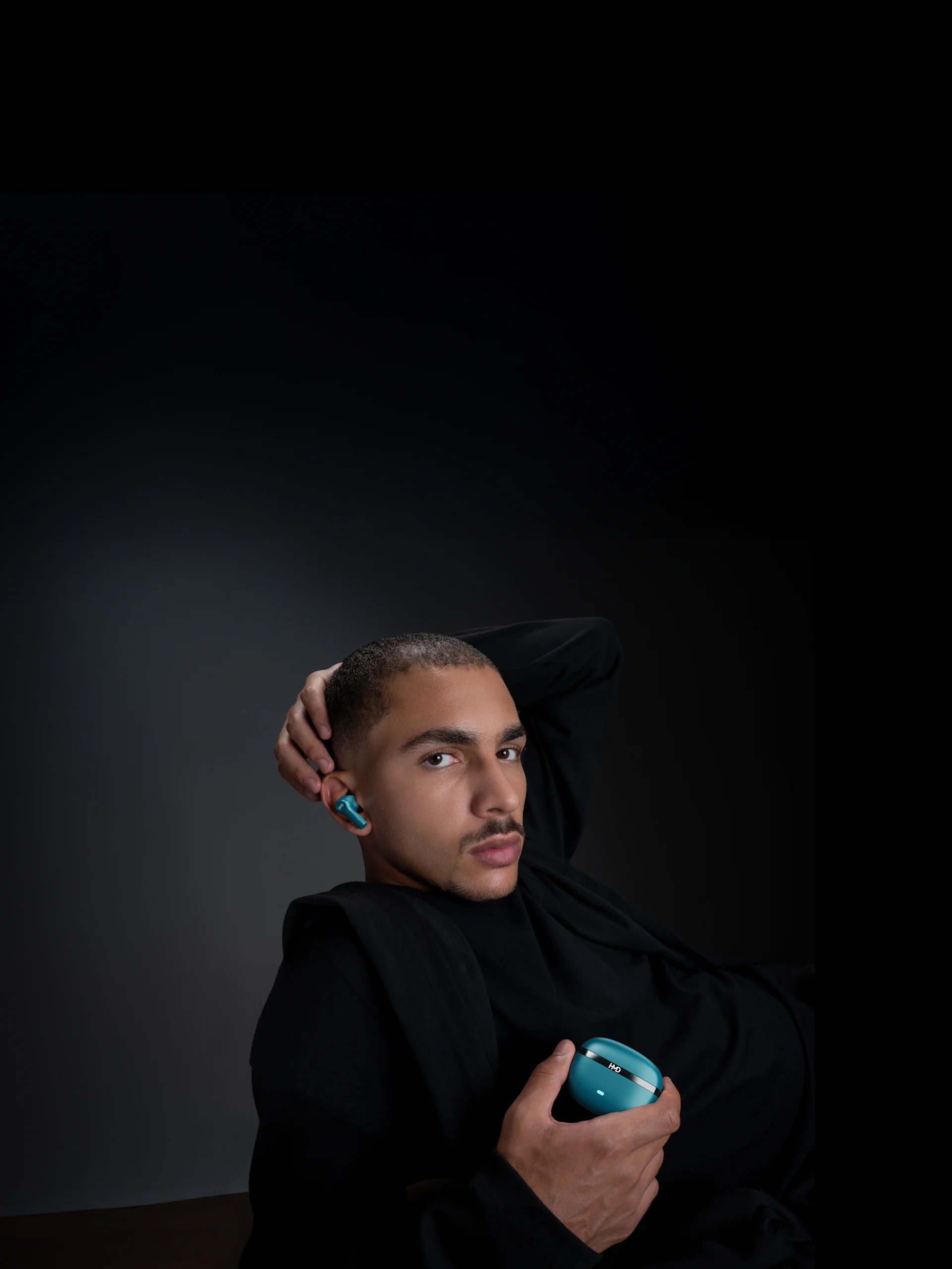 Man in black holding blue DUB X50 Pro earbuds case, wearing matching earbuds, against a dark background.