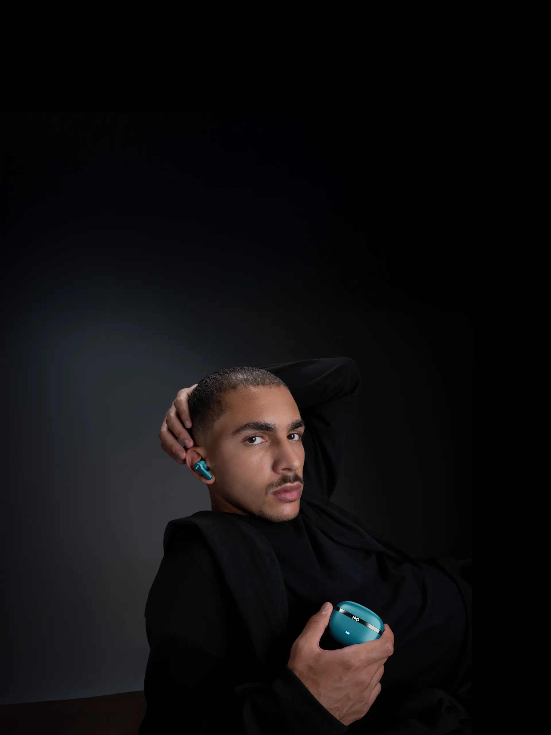 Man in black holding blue DUB X50 Pro earbuds case, wearing matching earbuds, against a dark background.
