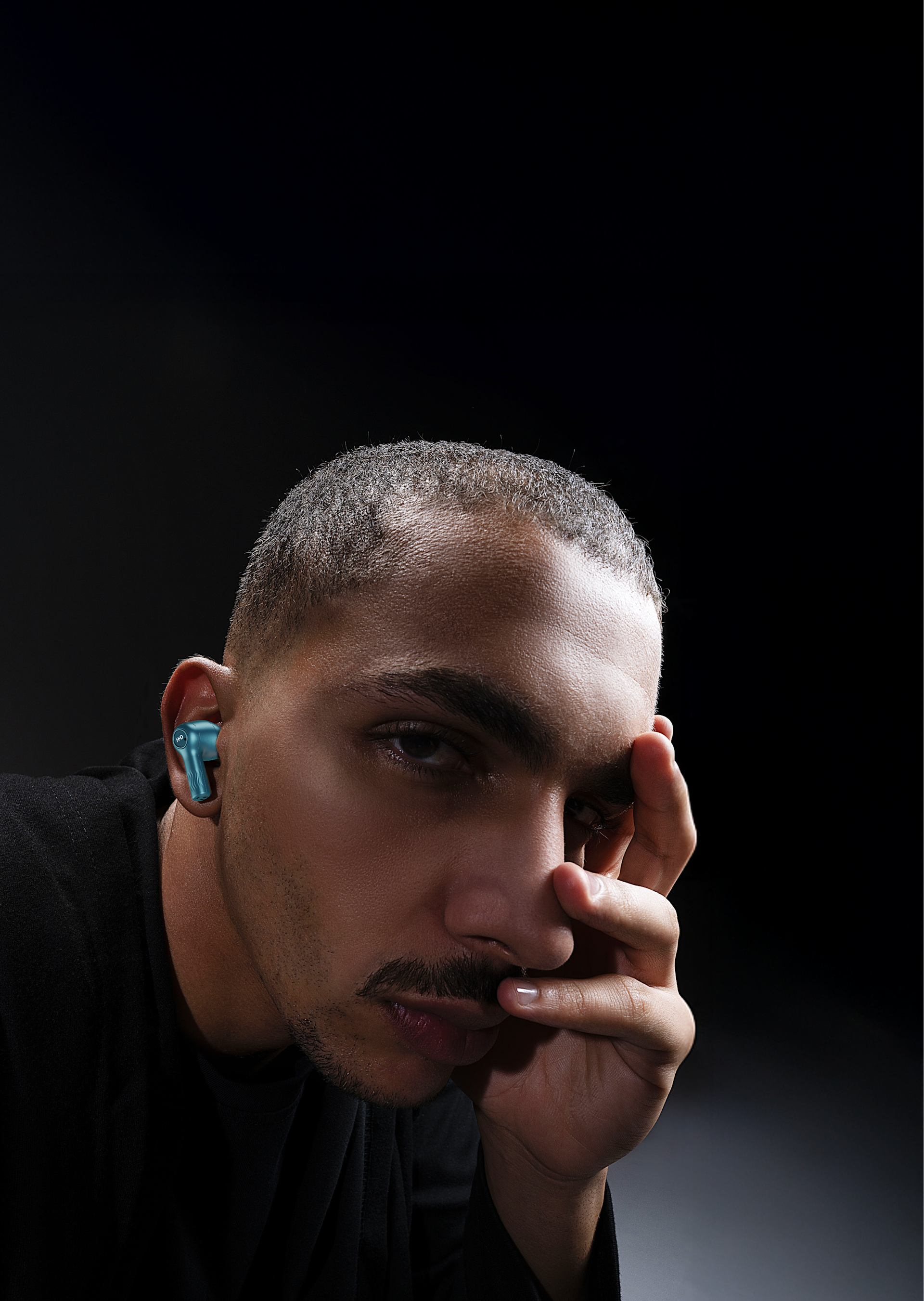 Man wearing HMD X50 Pro blue earbuds, resting his face on his hand, against a dark background.