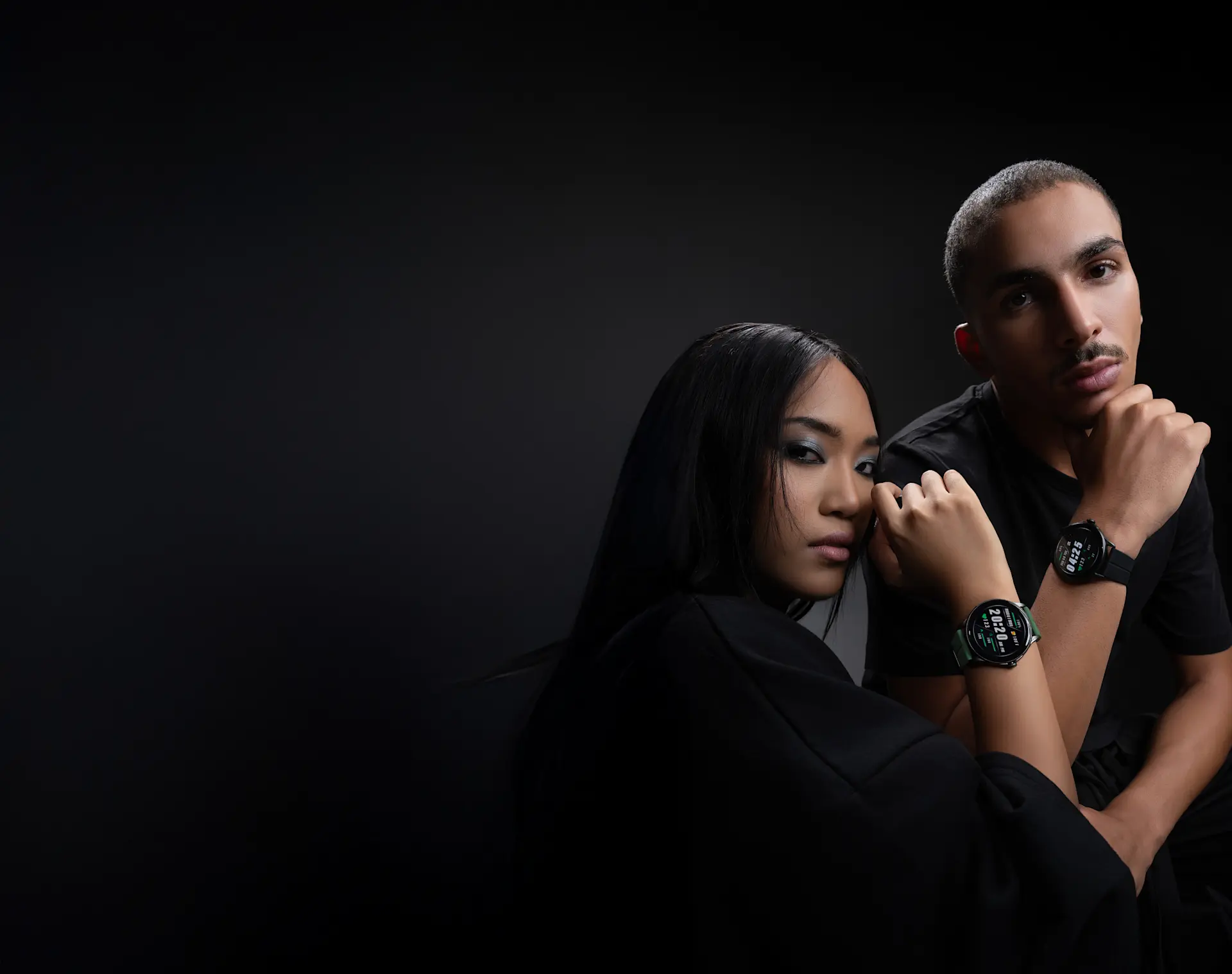 Two people in black outfits pose with HMD Watch X1 on their wrists against a dark background.