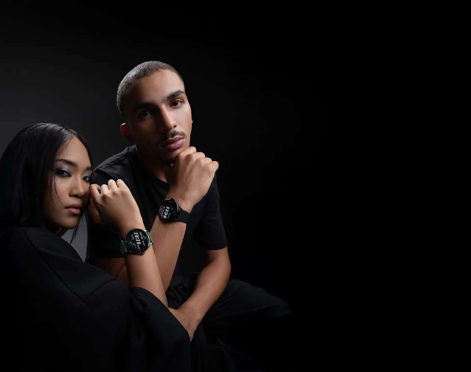 Two people in black outfits pose with HMD Watch X1 on their wrists against a dark background.