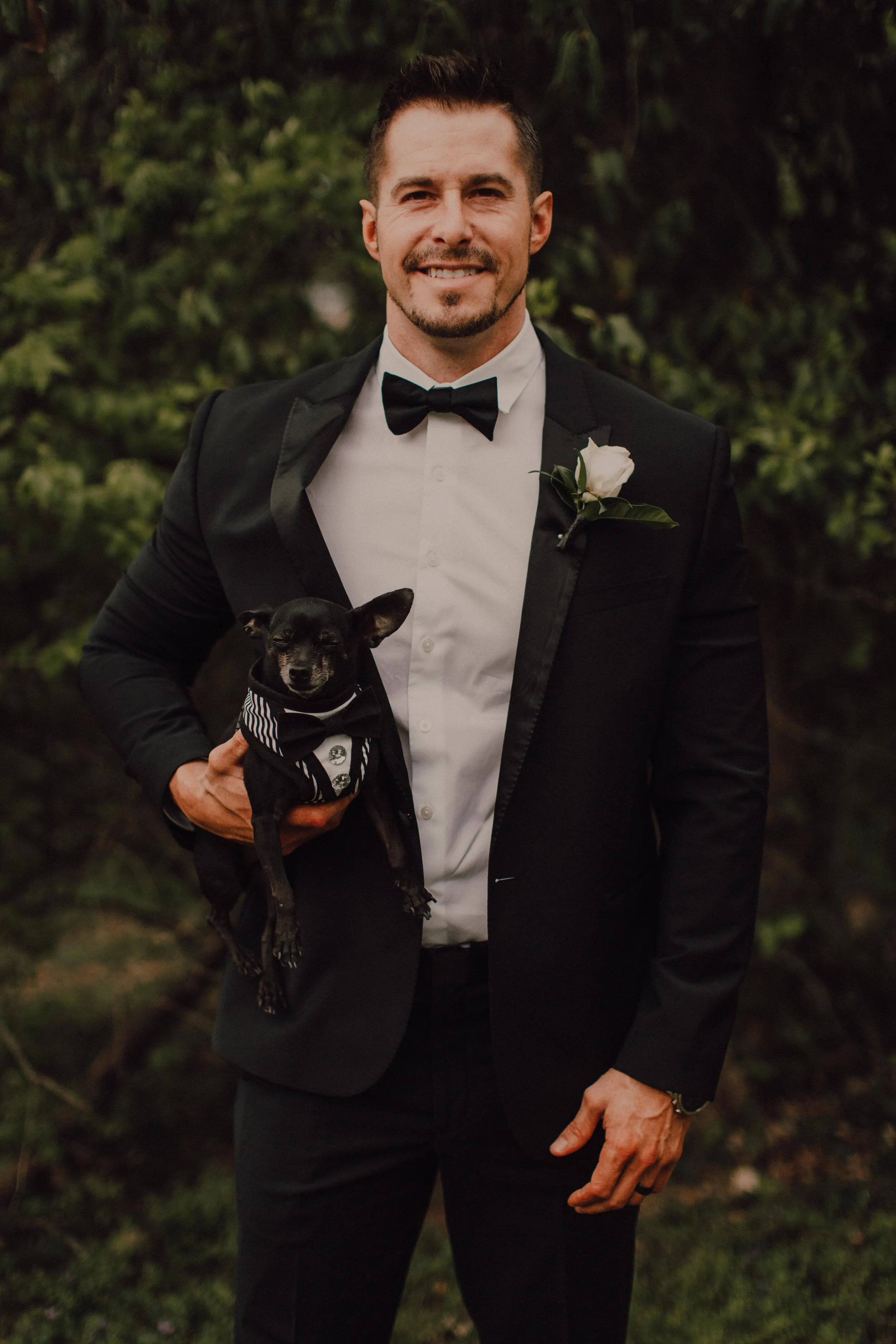 Groom standing with small dog at his wedding