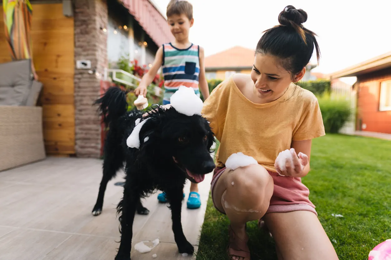 woman bathing dog in bath outside with child