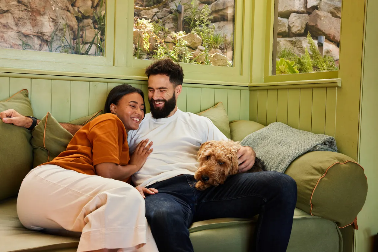 man and woman cuddling with dog on couch