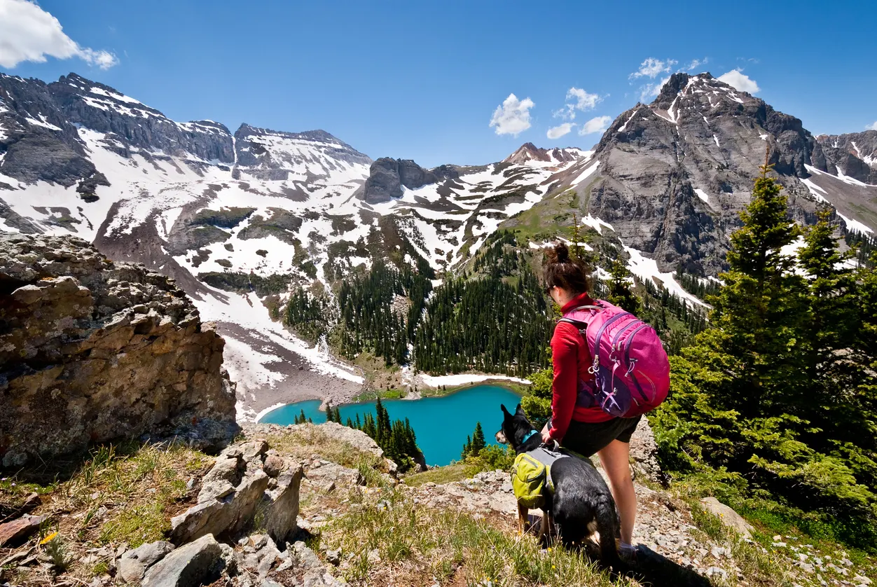 Dog and woman look out on colorado mountain mid-hike