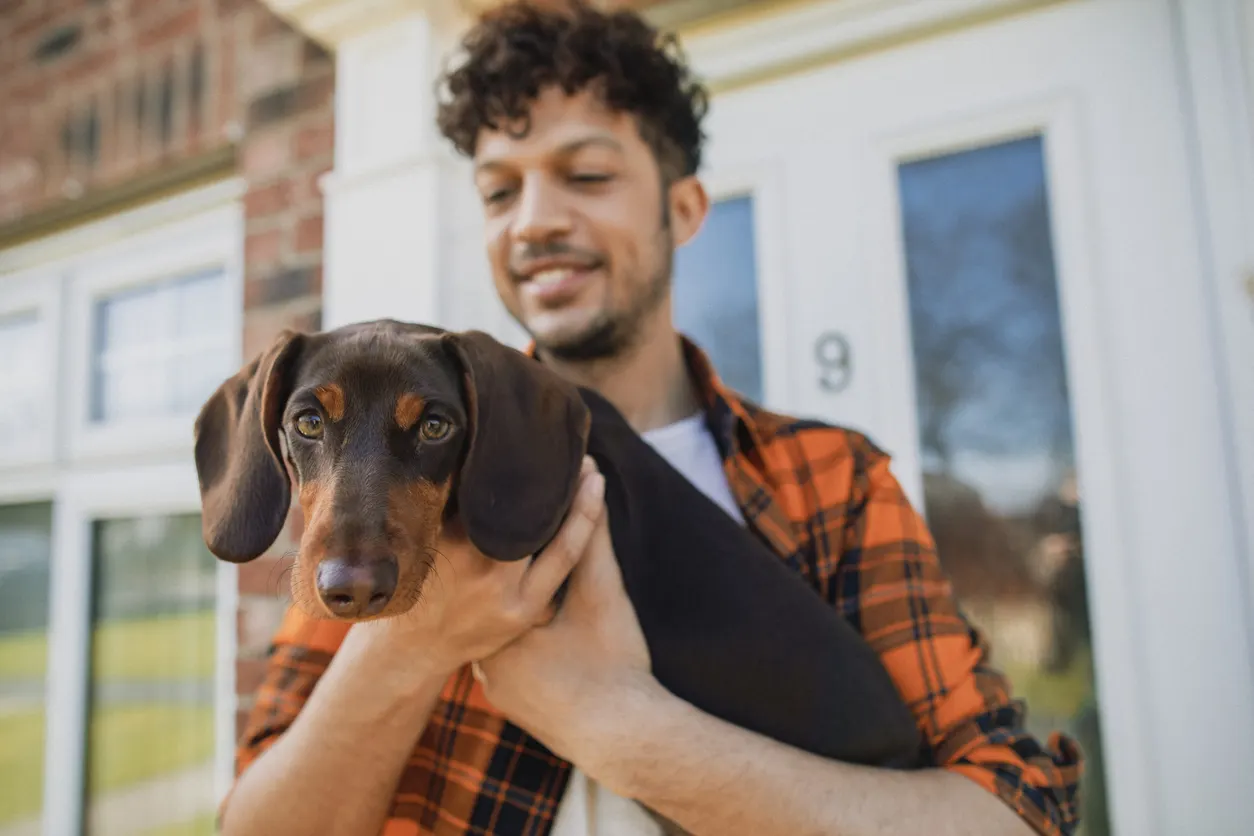 man holding small dog in front of house