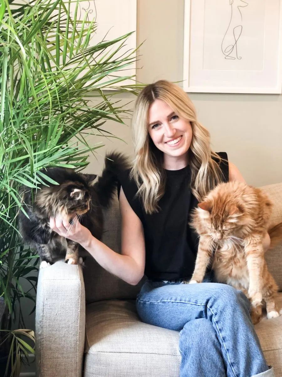 woman sitting on couch next to plant with two cats